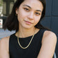 Woman wearing a black sleeveless top and gold necklace with a blurred background