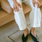 Person wearing white pants and black leather slipper shoes with a central seam and tulip shaped upper, a squared-off toe and 3/4" heel sitting on a couch.