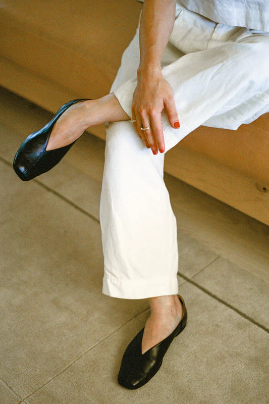 Person wearing white pants and black leather slipper shoe with central seam and tulip shaped upper with squared-off toe and 3/4" heel. 