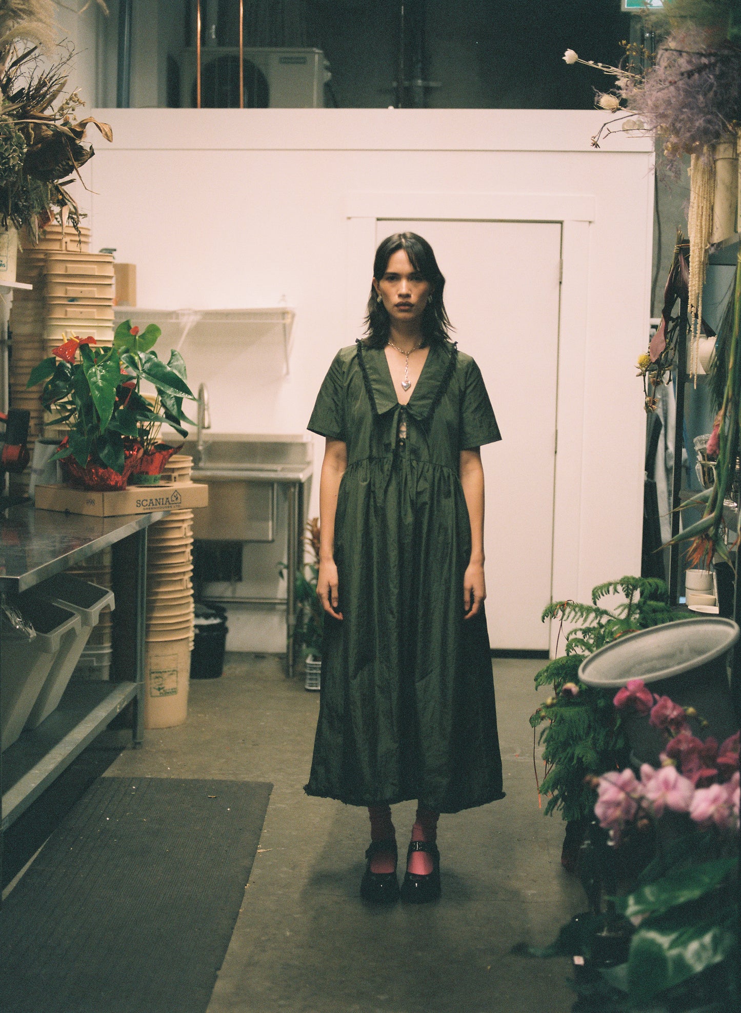 Woman in a green dress standing in a room with plants and furniture.