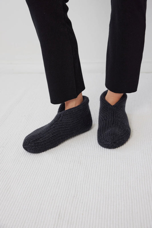 A pair of felted slippers in black color, worn by a person standing against a white background.