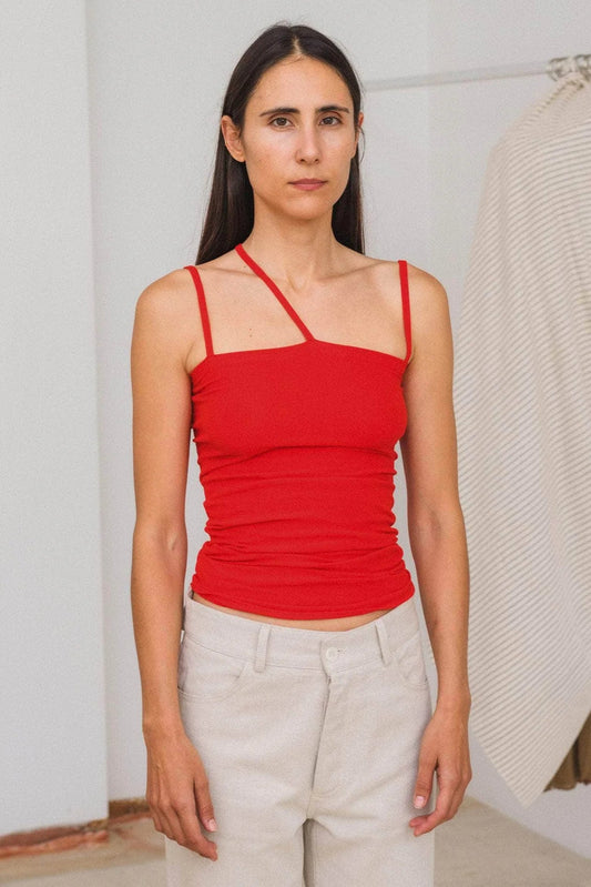 Woman wearing a red tank top and light-colored pants in a minimal indoor setting.