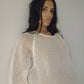 Close-up of Bohème Goods Fisherman Tee in cream showing open net cotton knit texture and relaxed fit, model leaning against a white wall