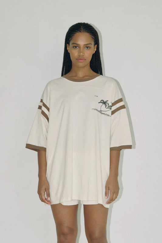 Bohème Goods Tourist Tee in cream full length front view showing oversized cotton silhouette, Club Bohème palm tree chest graphic and brown stripe sleeve detail, styled with matching Track Short