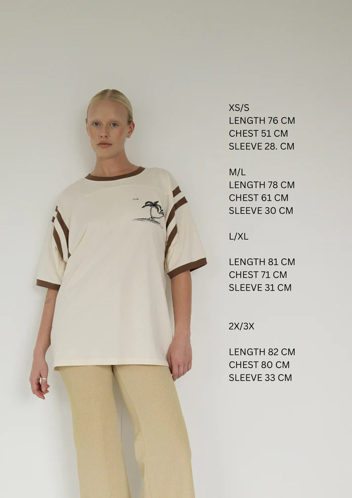 Bohème Goods Tourist Tee in cream size guide showing measurements for XS/S, M/L, L/XL and 2X/3X, styled with cream wide leg trousers