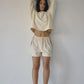 Bohème Goods Track Short in cream with brown side stripes worn with a cropped cream sweatshirt, arms raised, showing relaxed fit and drawstring waist against a white studio background