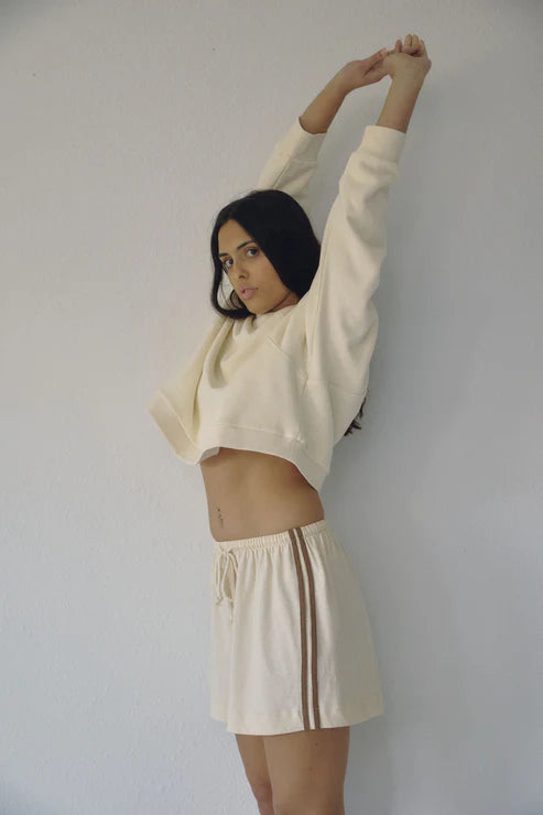 Side profile of Bohème Goods Track Short in cream showing vintage-inspired brown side stripe detail and relaxed cotton silhouette, styled with a cropped cream sweatshirt
