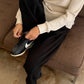 Le Bon Shoppe Waffle Lo Pants in true black worn seated on a brown sofa, styled with the cream Waffle Fundamental Tee and black sneakers, showing heavy waffle cotton texture