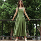Woman wearing a meadow green linen midi dress with scoop neckline and voluminous panier skirt, holding pink peonies — Vivienne Dress by Eliza Faulkner at Ånde