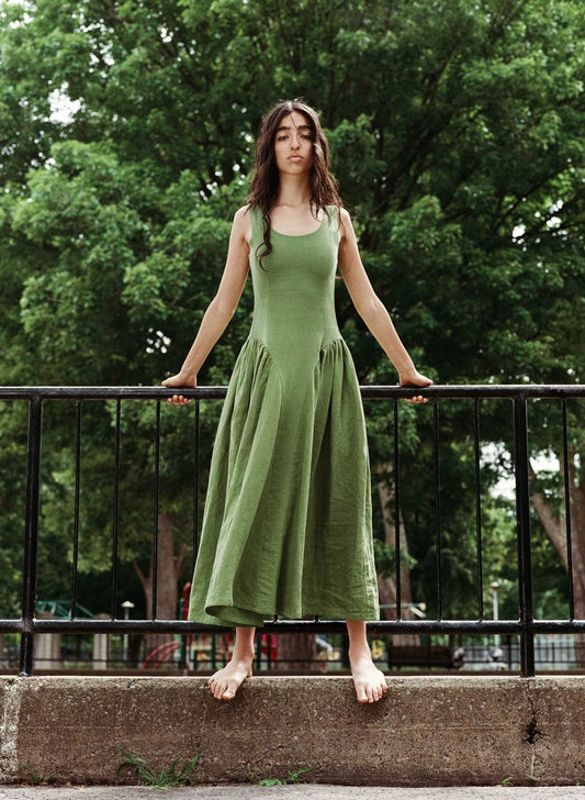 Woman wearing a meadow green linen midi dress with scoop neckline and voluminous panier skirt, holding pink peonies — Vivienne Dress by Eliza Faulkner at Ånde