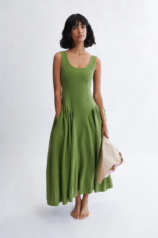 Woman wearing a meadow green linen midi dress with scoop neckline and voluminous panier skirt, holding pink peonies — Vivienne Dress by Eliza Faulkner at Ånde