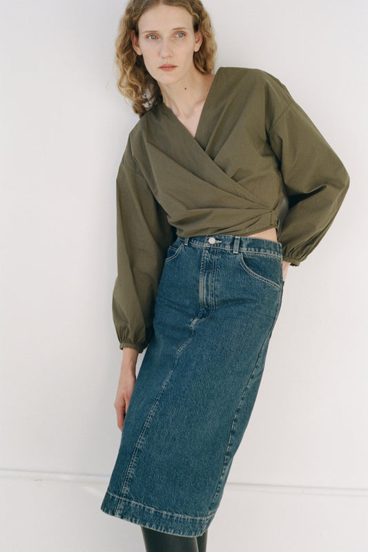 Woman wearing a green blouse and blue denim skirt against a white background