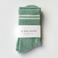Le Bon Shoppe Boyfriend Socks in meadow folded and banded with Le Bon Shoppe Boyfriend Socks packaging label, showing green ribbed cotton with white double stripe on a light grey surface