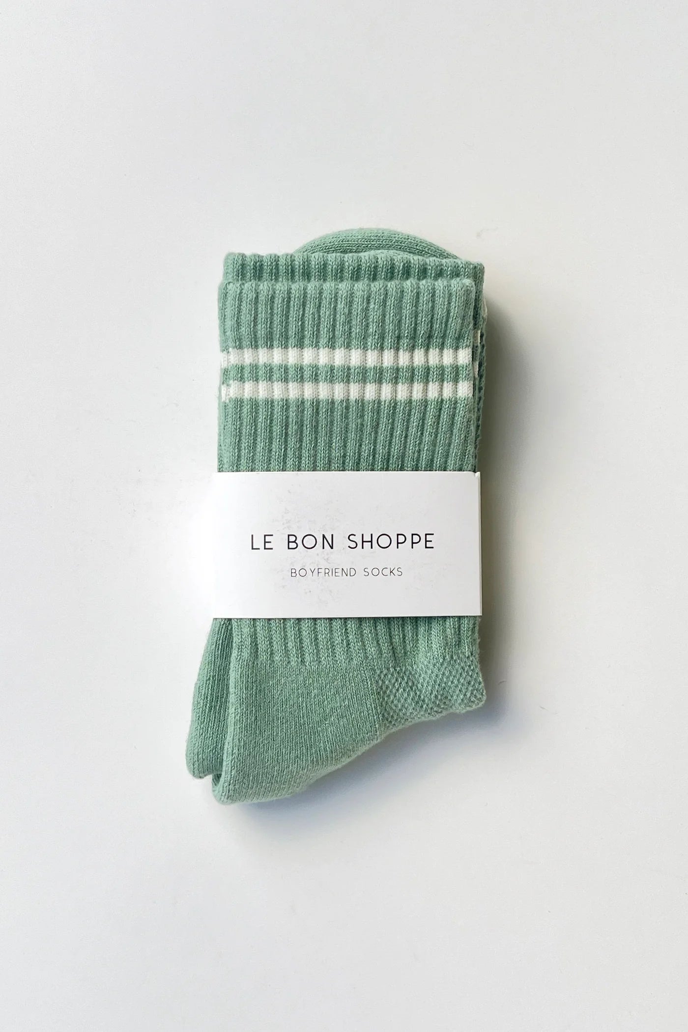 Le Bon Shoppe Boyfriend Socks in meadow folded and banded with Le Bon Shoppe Boyfriend Socks packaging label, showing green ribbed cotton with white double stripe on a light grey surface
