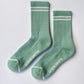 Pair of Le Bon Shoppe Boyfriend Socks in meadow laid flat showing sole with mesh panel, Le Bon Shoppe branding, contrast toe detail and white double stripe on green ribbed cotton