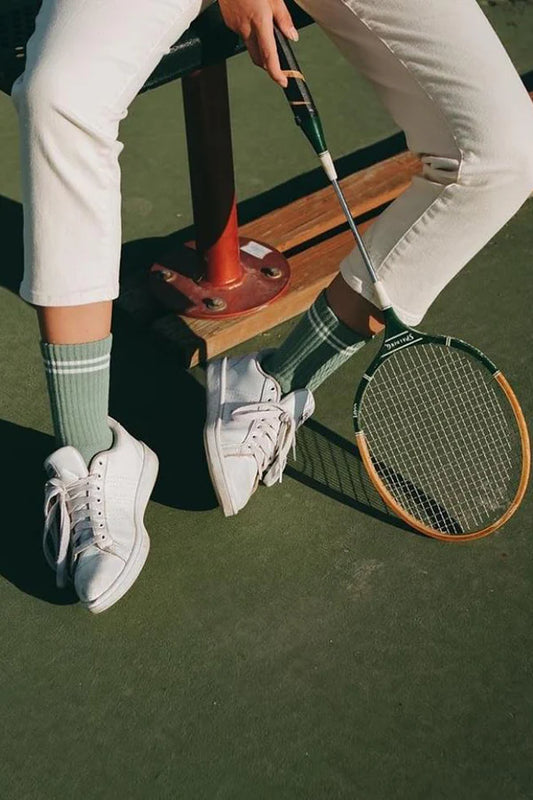 Le Bon Shoppe Boyfriend Socks in meadow worn on a tennis court with white sneakers and cream trousers, styled with a vintage wooden tennis racquet showing sporty vintage double stripe detail