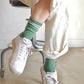 Le Bon Shoppe Boyfriend Socks in meadow worn with white sneakers and cream wide leg trousers, showing green ribbed cotton sock with white double stripe and longer-than-crew length