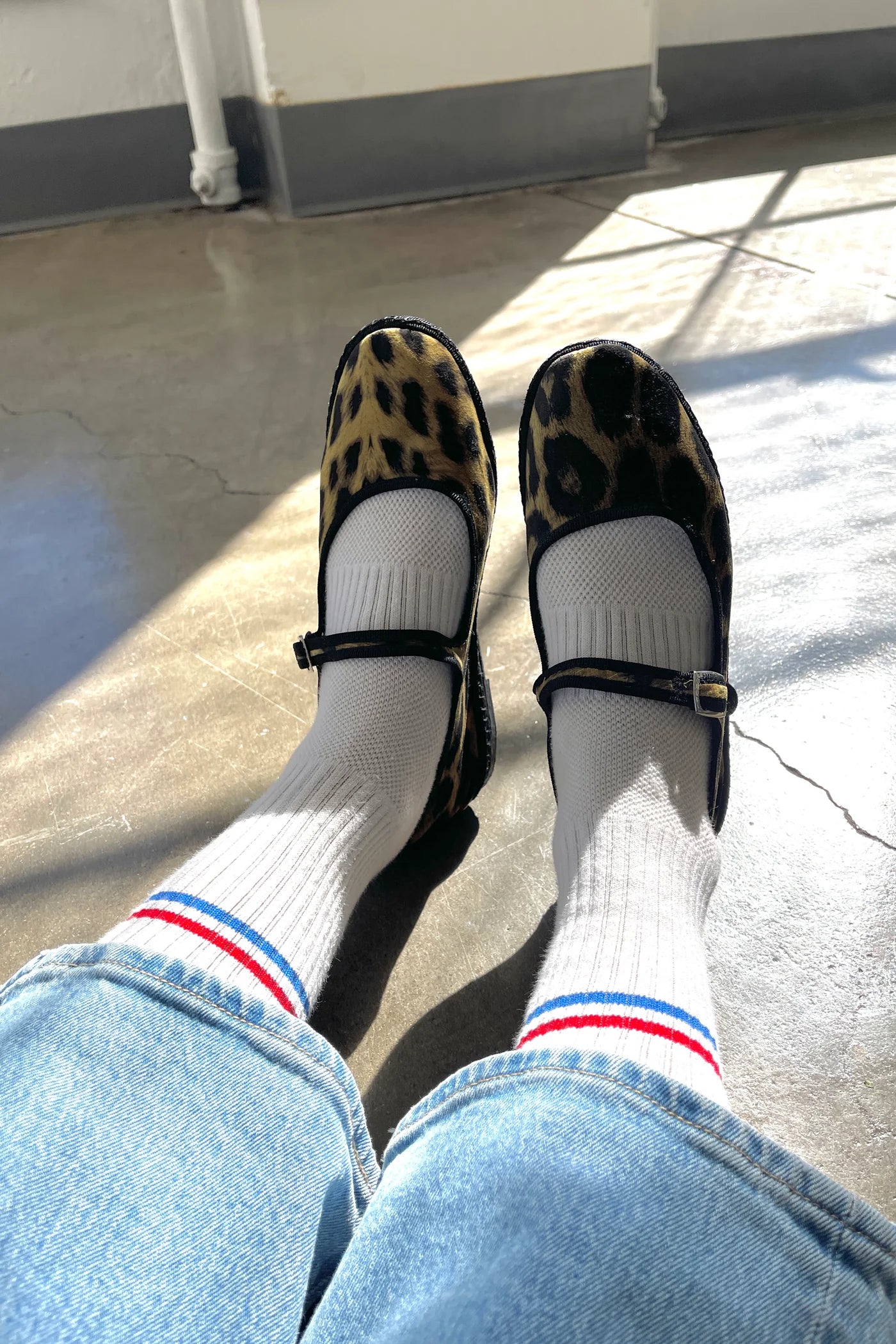 Le Bon Shoppe Boyfriend Socks in milk worn with leopard print Mary Jane flats and light wash jeans, showing white ribbed cotton sock with red and blue double stripe in natural sunlight