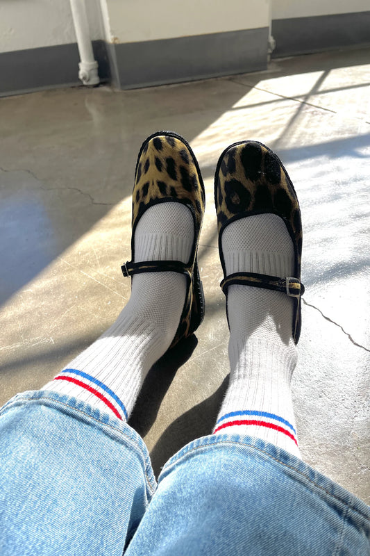 Le Bon Shoppe Boyfriend Socks in milk worn with leopard print Mary Jane flats and light wash jeans, showing white ribbed cotton sock with red and blue double stripe in natural sunlight
