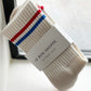Le Bon Shoppe Boyfriend Socks in milk packaged with Le Bon Shoppe Boyfriend Socks band, propped against a rain-streaked window showing red and blue double 