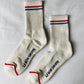 Pair of Le Bon Shoppe Boyfriend Socks in milk laid flat on white linen showing full longer-than-crew length, red and blue double stripe, Le Bon Shoppe sole 