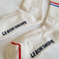 Close-up of Le Bon Shoppe Boyfriend Socks in milk showing sole branding, red contrast toe detail and red and blue double stripe on white ribbed cotton, laid on white linen