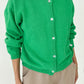 Le Bon Shoppe Cotton Leila Cardigan in spring green buttoned up over a cobalt blue tee and cream trousers, showing shell button detail and relaxed knit texture