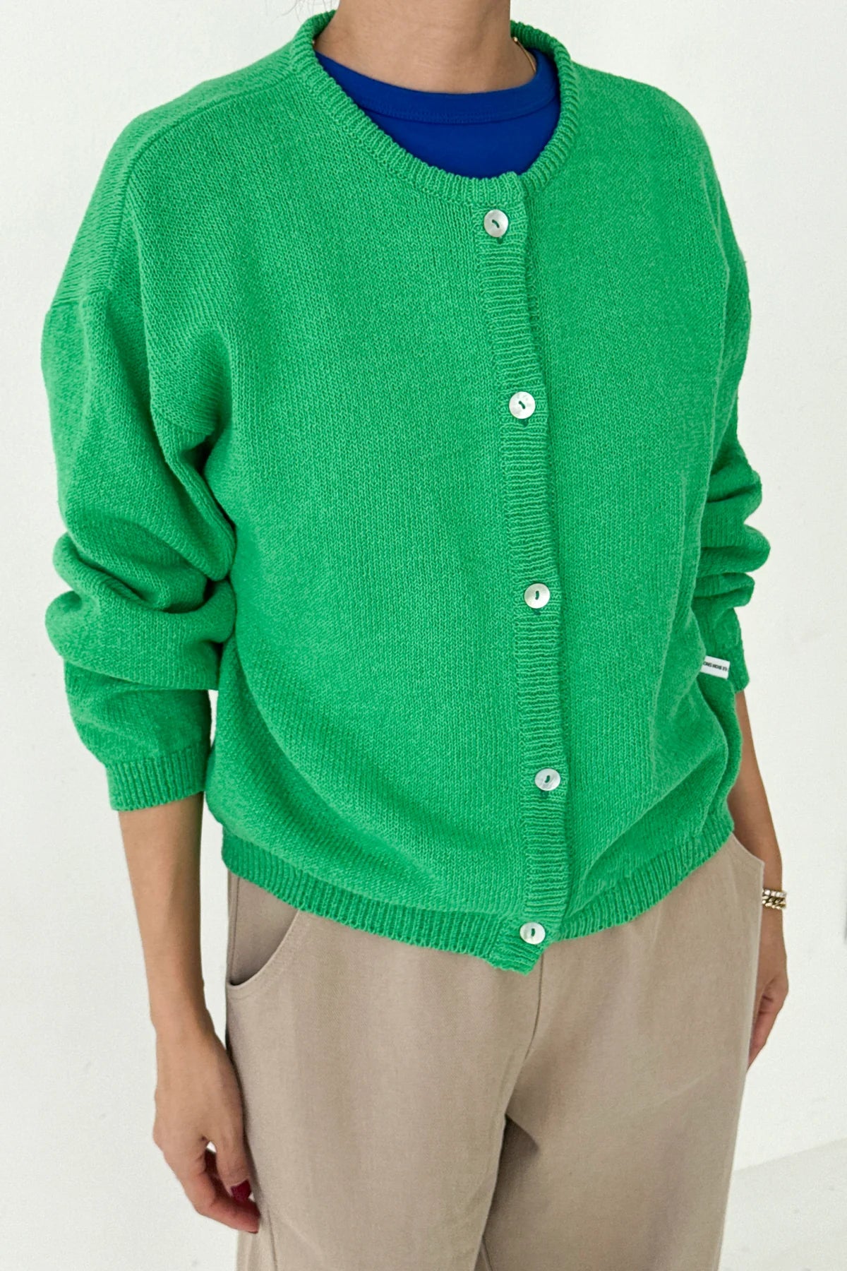 Le Bon Shoppe Cotton Leila Cardigan in spring green buttoned up over a cobalt blue tee and cream trousers, showing shell button detail and relaxed knit texture