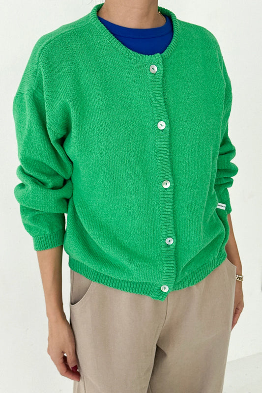 Le Bon Shoppe Cotton Leila Cardigan in spring green buttoned up over a cobalt blue tee and cream trousers, showing shell button detail and relaxed knit texture
