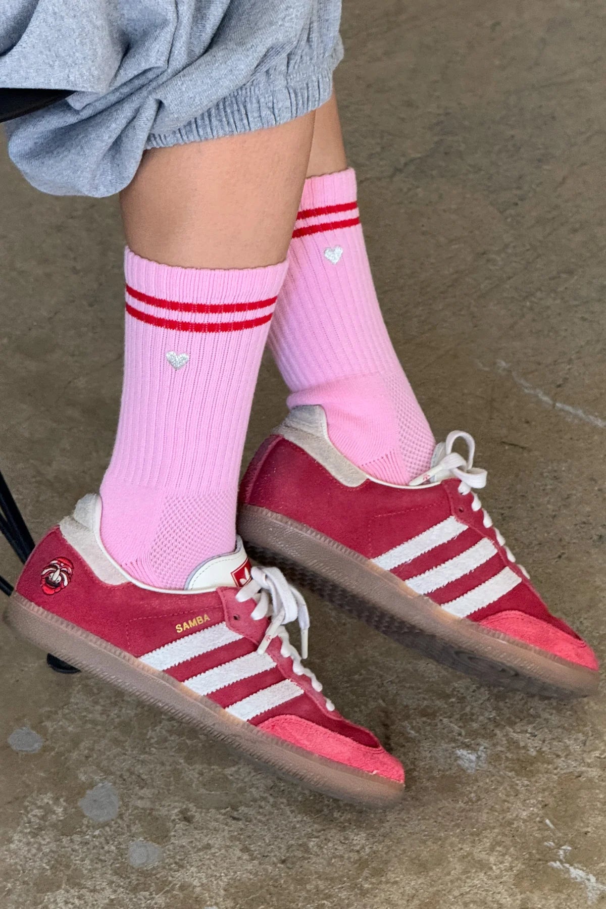 Le Bon Shoppe Embroidered Boyfriend Socks in amour pink worn with red Adidas Samba sneakers and grey sweat shorts, showing pink ribbed cotton with red double stripe and embroidered heart detail