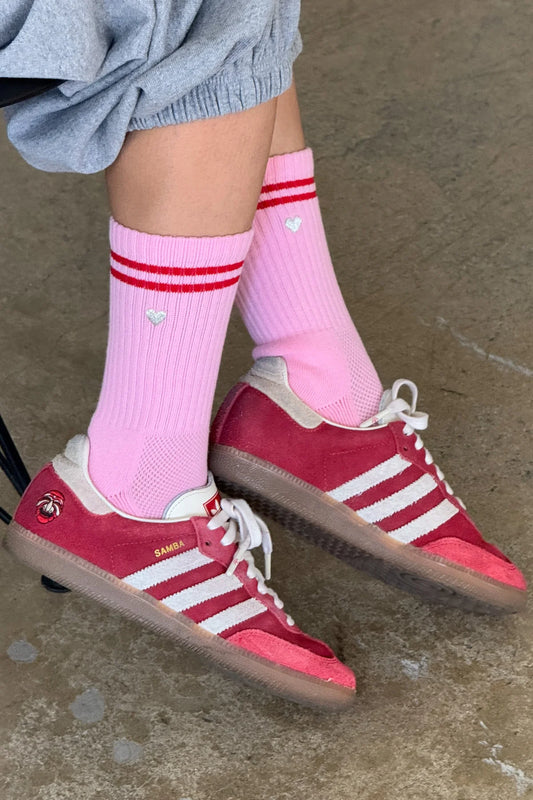 Le Bon Shoppe Embroidered Boyfriend Socks in amour pink worn with red Adidas Samba sneakers and grey sweat shorts, showing pink ribbed cotton with red double stripe and embroidered heart detail