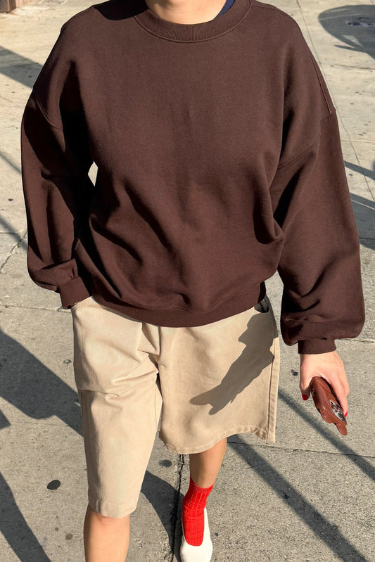 Le Bon Shoppe French Terry Core Sweatshirt in cocoa bean worn with taupe shorts, red ribbed socks and white shoes, shot on a sunny street