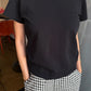 e Bon Shoppe Go-To Tee in true black partially tucked into black and white gingham trousers, showing longer length and slightly curved hem with relaxed cotton jersey fit