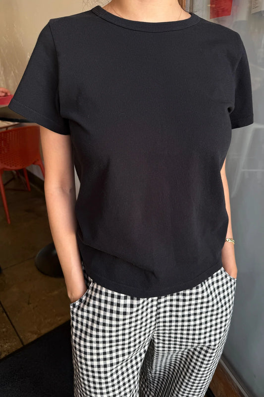 e Bon Shoppe Go-To Tee in true black partially tucked into black and white gingham trousers, showing longer length and slightly curved hem with relaxed cotton jersey fit