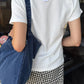 Back view of Le Bon Shoppe Go-To Tee in vintage white styled with black and white gingham trousers and a denim tote bag, Le Bon Shoppe hang tag visible at neckline
