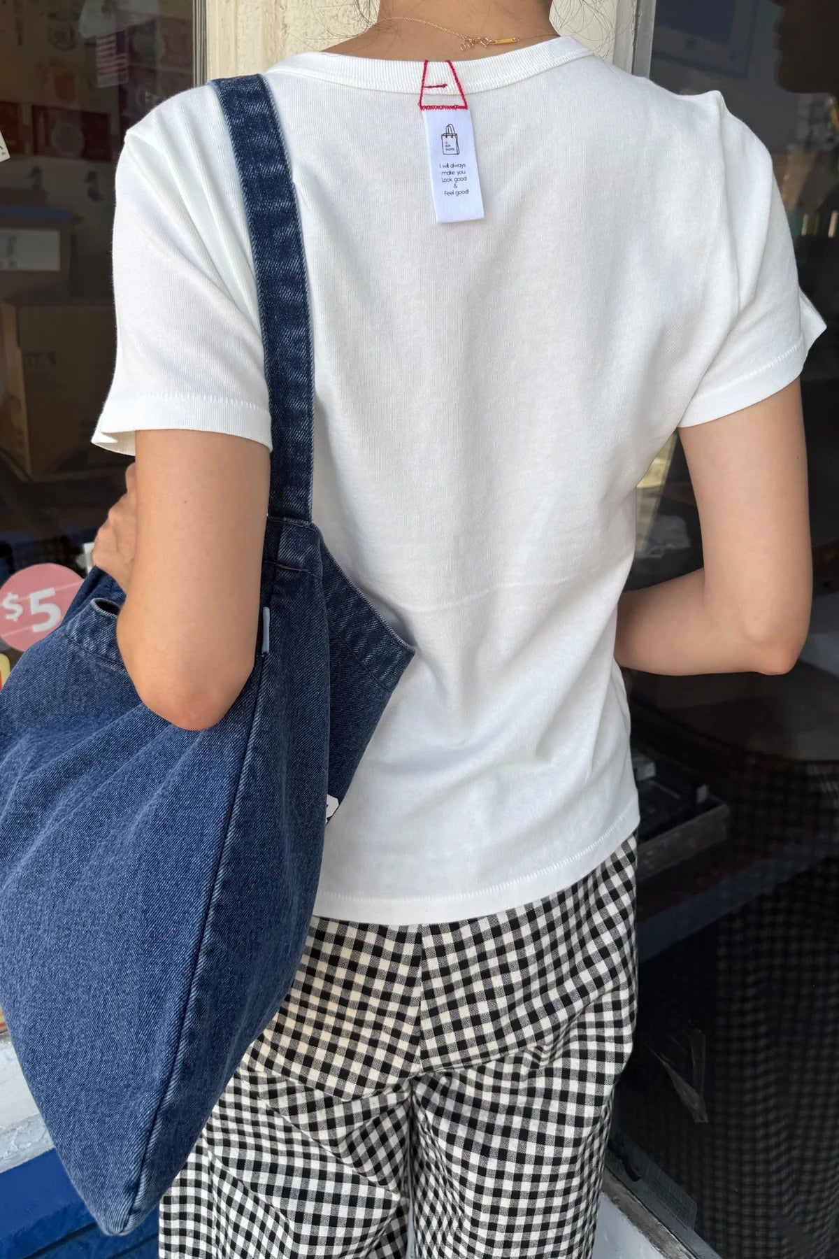 Back view of Le Bon Shoppe Go-To Tee in vintage white styled with black and white gingham trousers and a denim tote bag, Le Bon Shoppe hang tag visible at neckline
