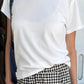 Le Bon Shoppe Go-To Tee in vintage white worn untucked over black and white gingham trousers with a denim tote bag, showing relaxed longer length and slightly curved hem