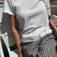 Le Bon Shoppe Go-To Tee in vintage white worn seated on a white chair in sunlight, styled with black and white gingham trousers and a denim bag
