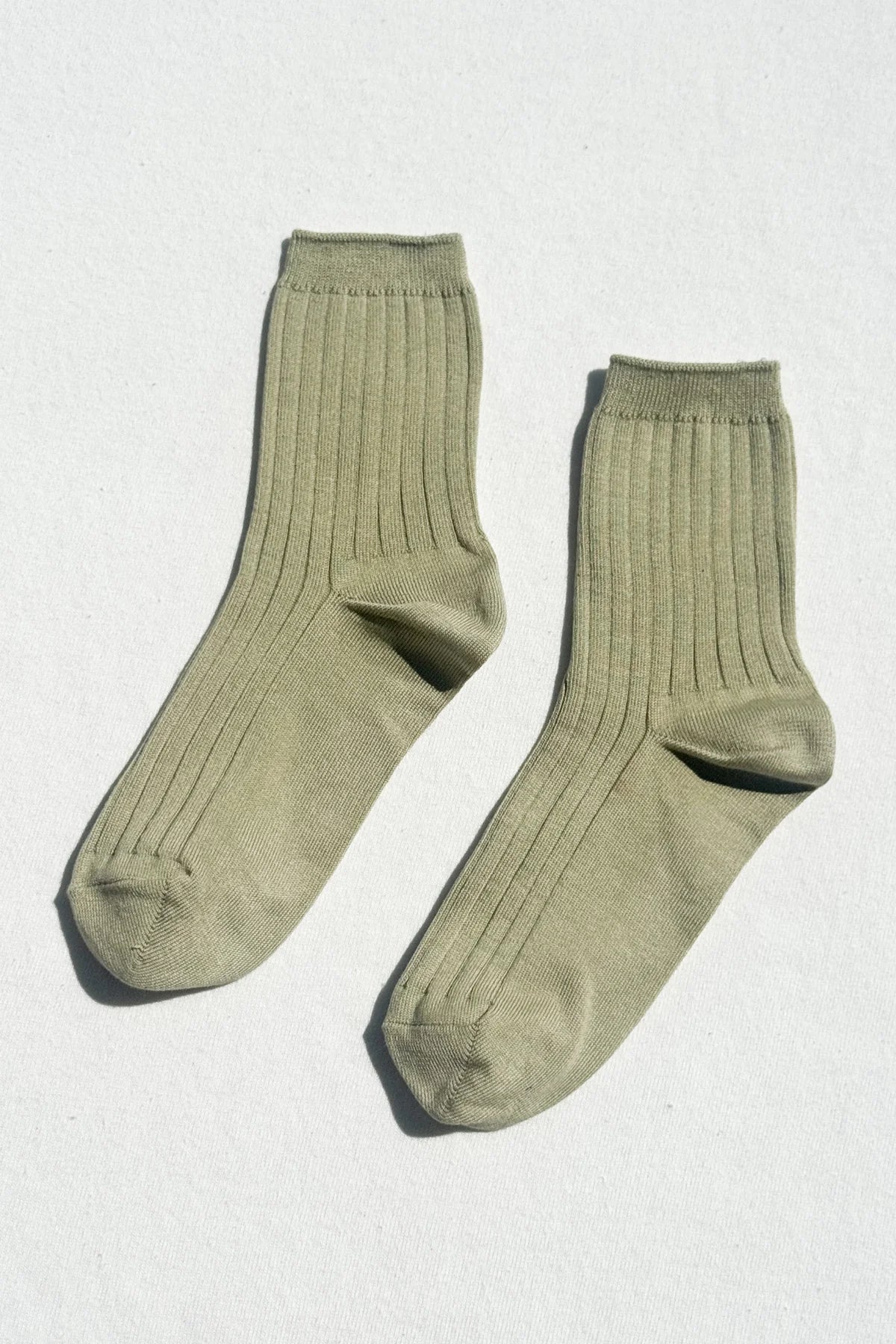 Pair of Le Bon Shoppe Her Socks in avocado green laid flat on a white surface, showing the ribbed cotton-blend texture and quarter-crew length