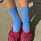 Le Bon Shoppe Her Socks in periwinkle worn front-on with red mesh jelly ballet flats, showing ribbed cotton-blend texture and quarter-crew length against a concrete pavement