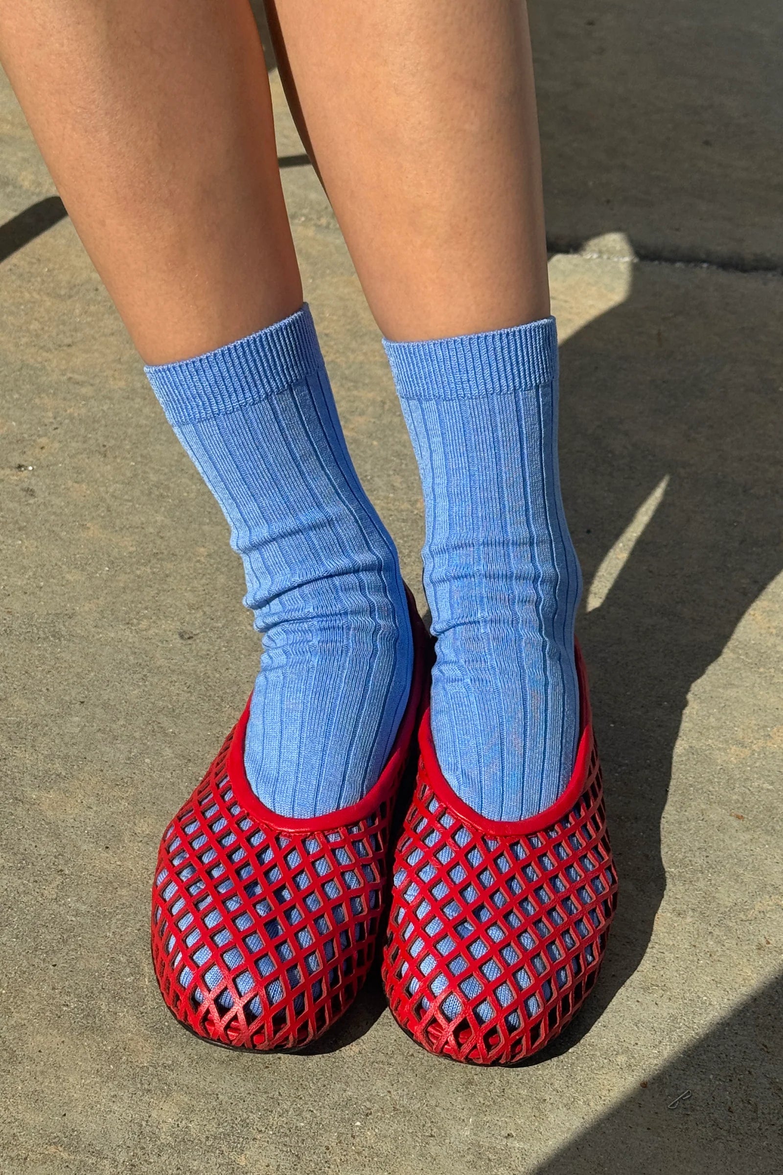 Le Bon Shoppe Her Socks in periwinkle worn front-on with red mesh jelly ballet flats, showing ribbed cotton-blend texture and quarter-crew length against a concrete pavement