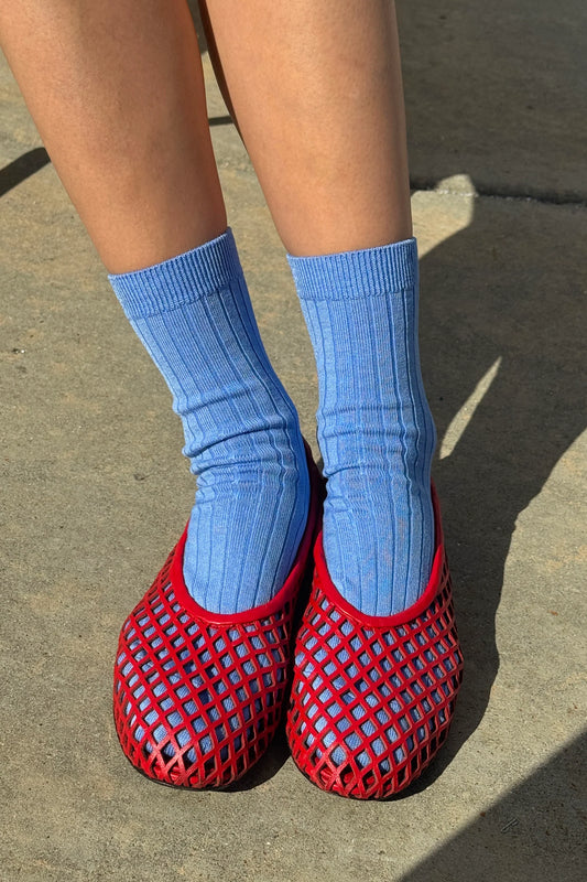 Le Bon Shoppe Her Socks in periwinkle worn front-on with red mesh jelly ballet flats, showing ribbed cotton-blend texture and quarter-crew length against a concrete pavement