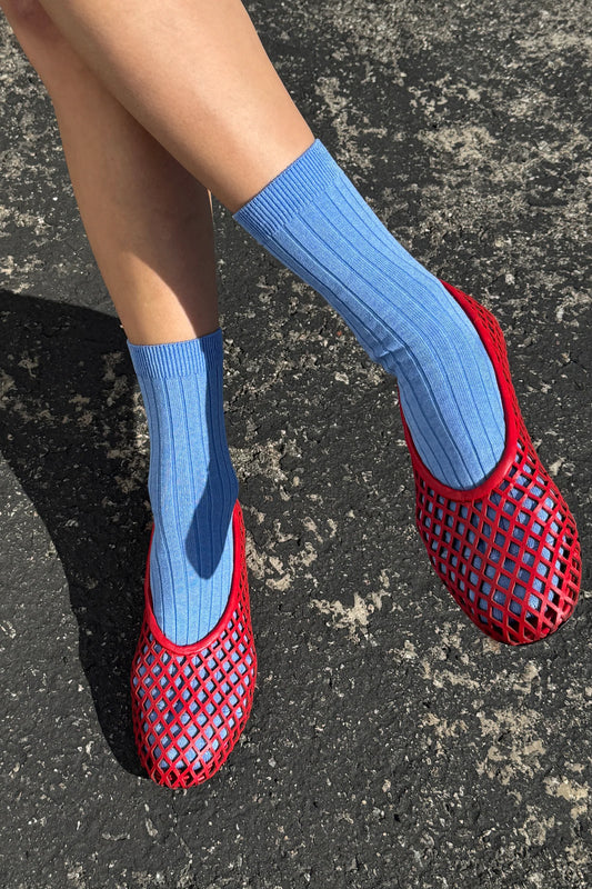 Le Bon Shoppe Her Socks in periwinkle worn with red mesh jelly ballet flats on dark asphalt, showing ribbed cotton-blend texture and quarter-crew length in natural sunlight