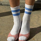 Le Bon Shoppe Her Varsity Socks in periwinkle straight-on view with pink open-toe heels, showing full quarter-crew length and periwinkle double stripe on white ribbed cotton-blend