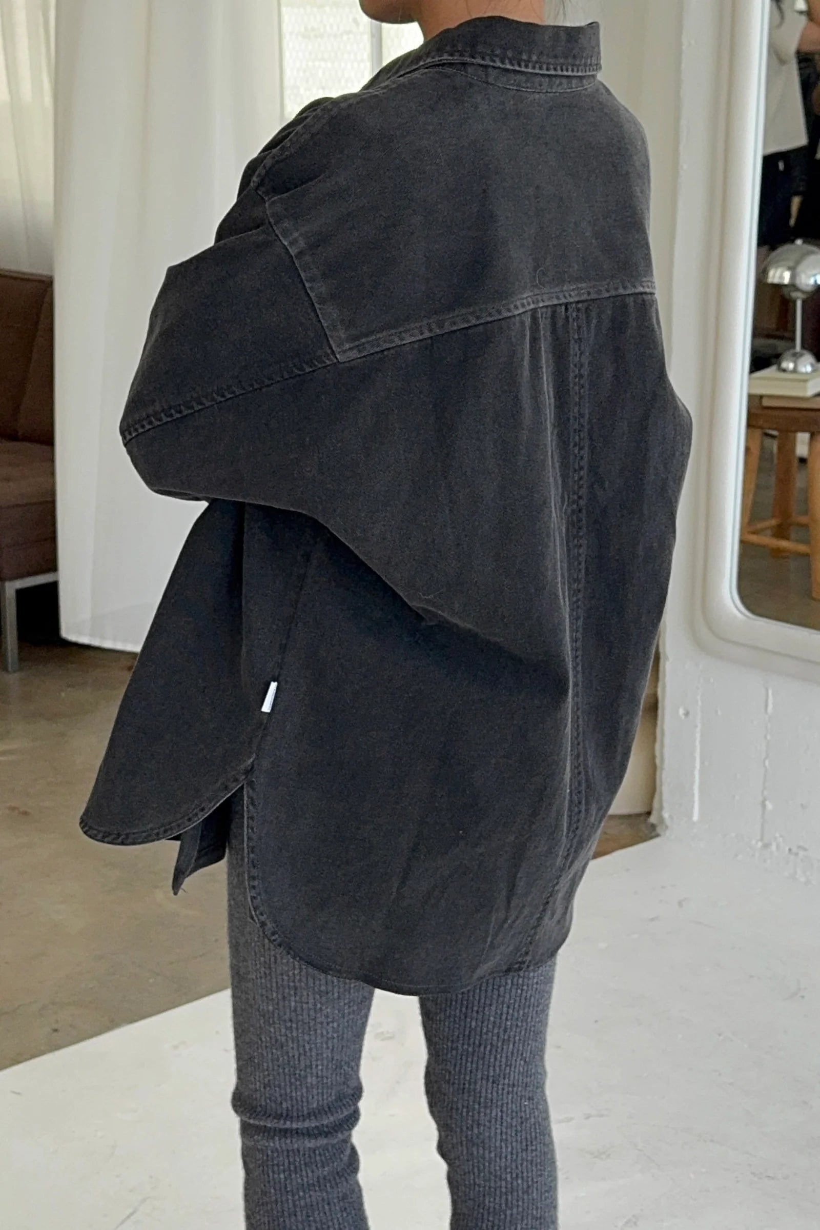 Back view of Le Bon Shoppe Theo Jacket in black denim showing rounded hem, yoke seam detail and oversized silhouette, styled with dark ribbed knit trousers