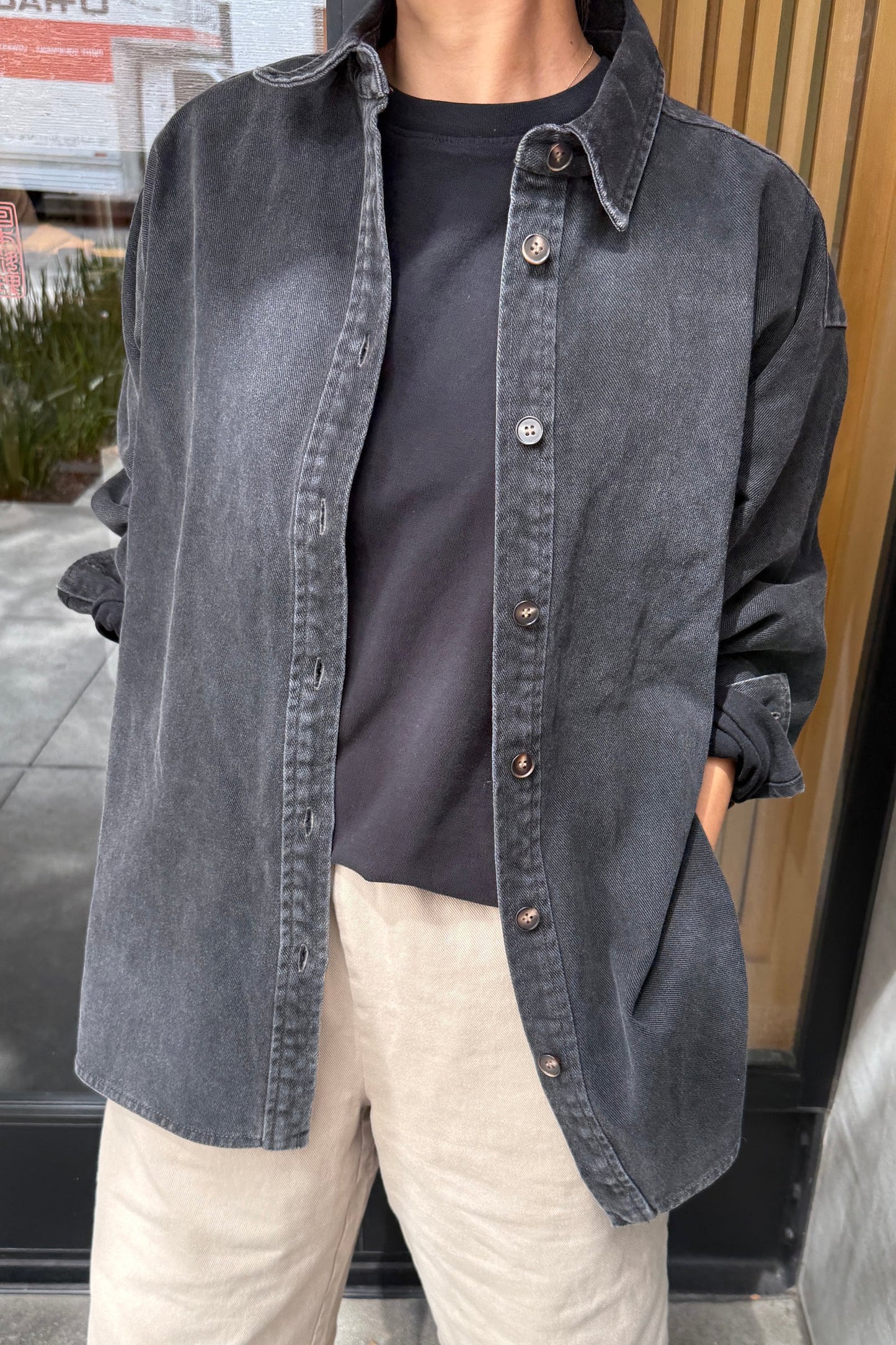 Close-up of Le Bon Shoppe Theo Jacket in black denim showing button front placket and contrast stitching, layered over a black tee with cream trousers