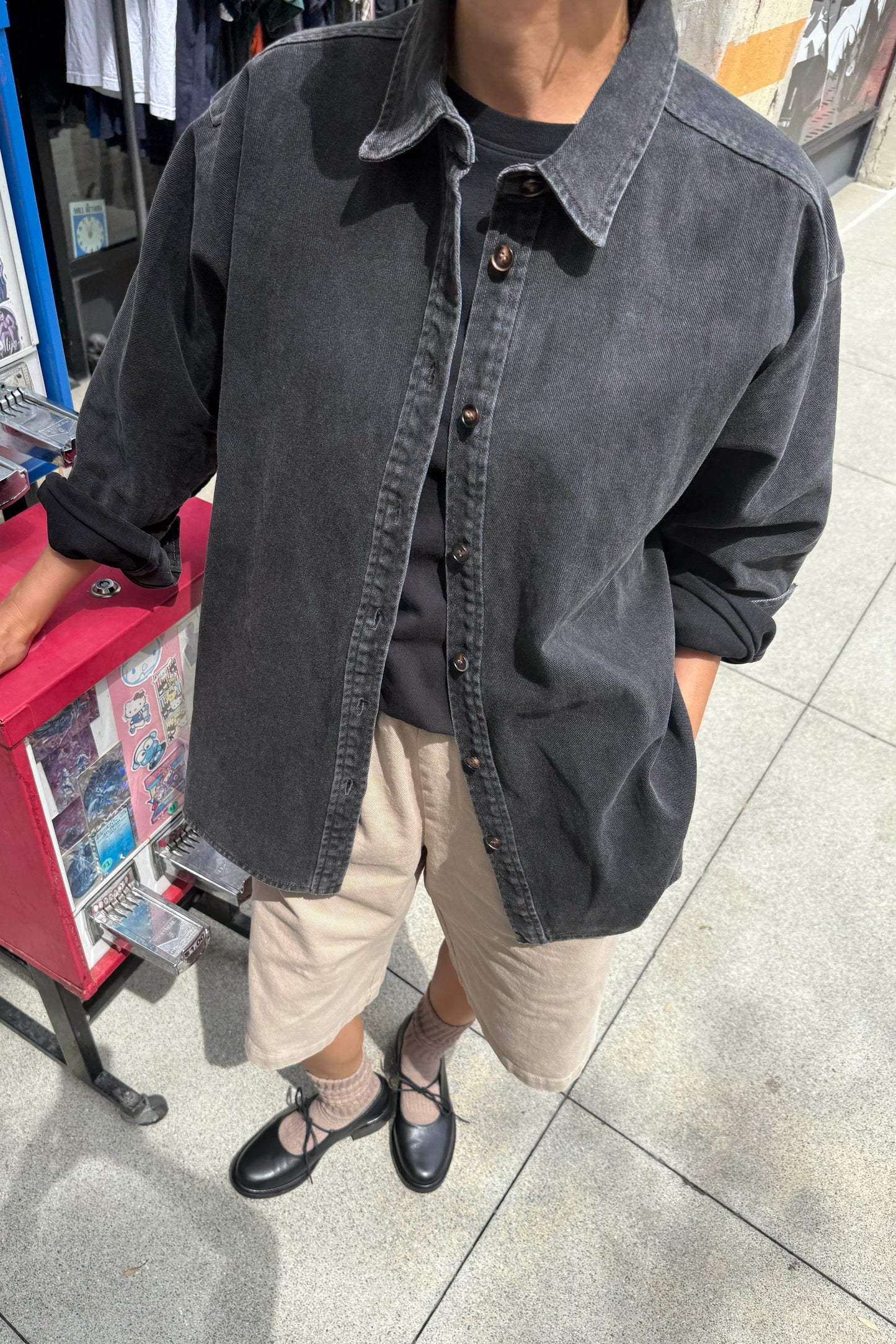 Le Bon Shoppe Theo Jacket in black denim worn open over a black tee and cream shorts with black ballet flats, shot on a city street