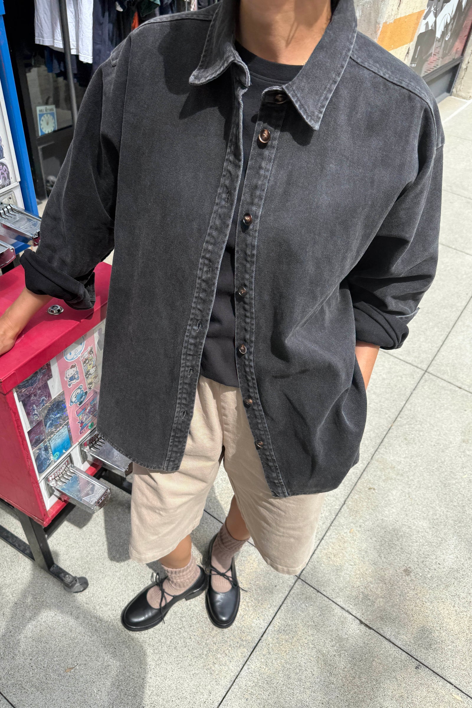 Le Bon Shoppe Theo Jacket in black denim worn open over a black tee and cream shorts with black ballet flats, shot on a city street