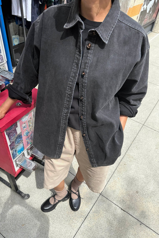 Le Bon Shoppe Theo Jacket in black denim worn open over a black tee and cream shorts with black ballet flats, shot on a city street