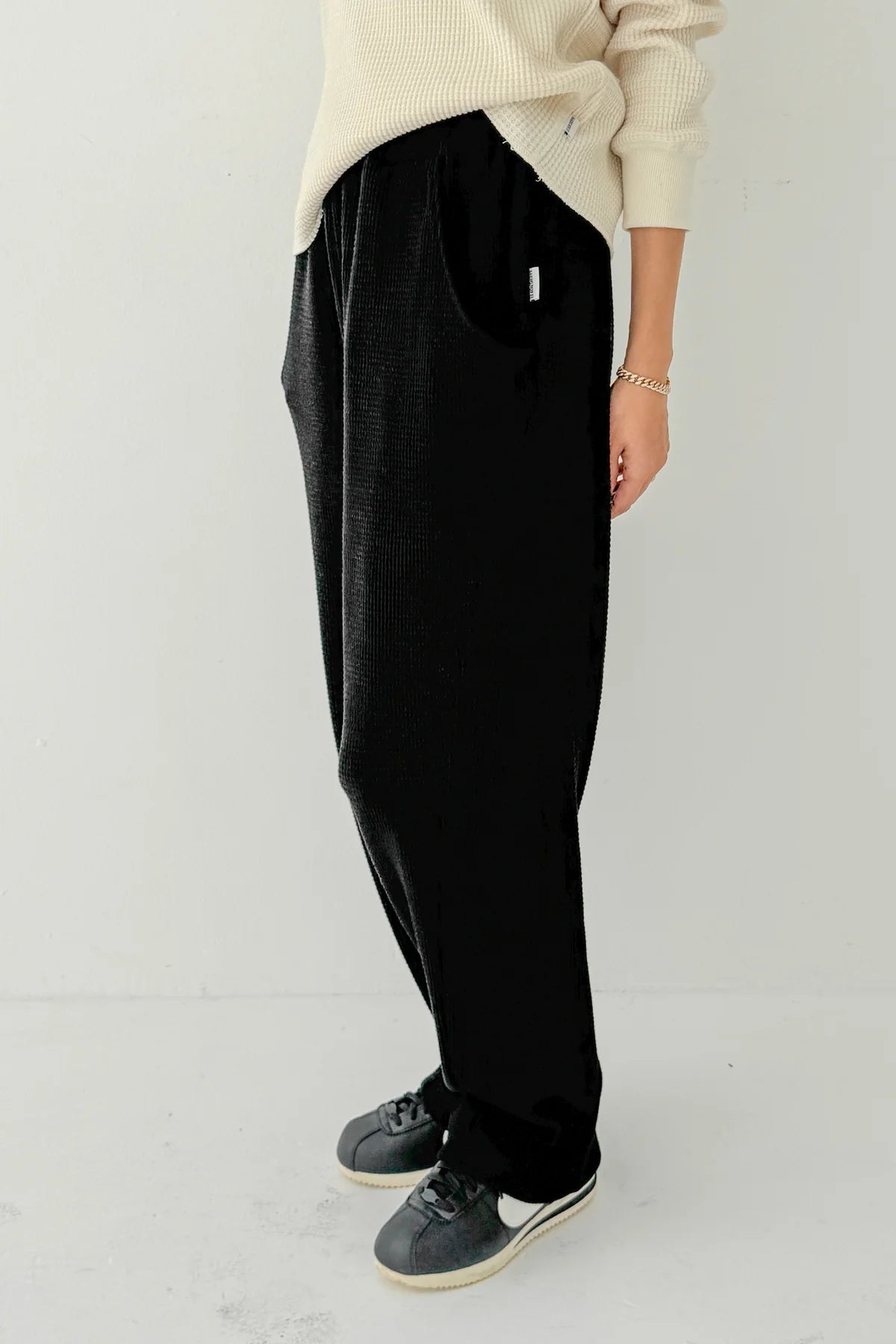 Side profile of Le Bon Shoppe Waffle Lo Pants in true black showing signature arc seam detail, elastic waistband and relaxed silhouette, styled with cream Waffle Fundamental Tee